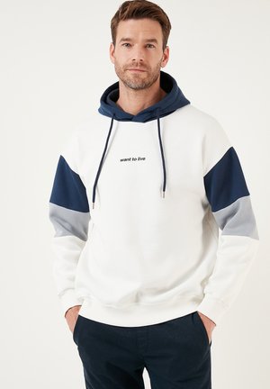 White hoodie with navy blue and gray sleeves. Text "want to live" on the front. Features adjustable drawstring and ribbed cuffs.