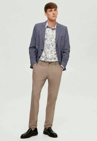 Ελαφρύ μπλε σακάκι πάνω από λευκό πουκάμισο με λουλούδια, σε συνδυασμό με μπεζ παντελόνι και μαύρες παπούτσια. Απλός σχεδιασμός, κομψή γραμμή, ουδέτερα χρώματα.