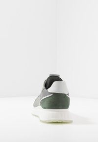 Scarpa sportiva grigia e verde con tomaia in suede texturizzato e mesh, accentuazione bianca sul tallone e una suola spessa bianca. Vista posteriore mostrata.
