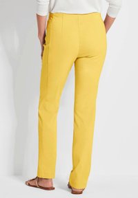 Geel recht gesneden broek met een hoge taille, voorzien van gestikte details aan de voorkant en een gladde textuur, gecombineerd met platte sandalen.