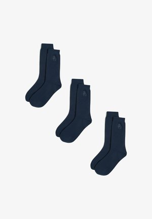 Tumed sinised sokid siledast kangast, ribadega varruka ja diskreetse logoga pahkluu lähedal. Kolm paari on kenasti paigutatud.