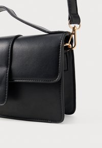 Saco crossbody em pele sintética preta com fecho de aba, detalhes em metal dourado e uma textura suave; inclui uma alça de ombro removível.