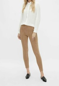 Lekka, biała koszula z długim rękawem zapinana na guziki, zestawiona z beżowymi legginsami z imitacji zamszu i czarnymi mokasynami, prezentująca smukłe dopasowanie.