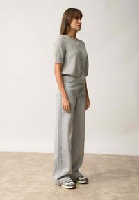 Jasnoszara, dziergana kardiganka z krótkimi rękawami i zapięciem na guziki, zestawiona z dżinsami o wysokim stanem i szerokimi nogawkami w dopasowanym odcieniu szarości oraz sneakersami.