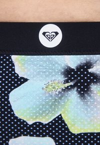 Ζώνη από ύφασμα με ανθρακικό μοτίβο σε αποχρώσεις μπλε, πράσινο και μαύρο, με μια μαύρη ταινία στο κέντρο που φέρει λευκό κυκλικό λογότυπο.