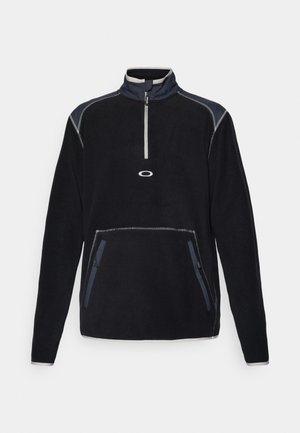 Fleece genser i svart med høy krage, halvlyslukking foran, to sidelommer og kontrastsøm i grått og marineblått.