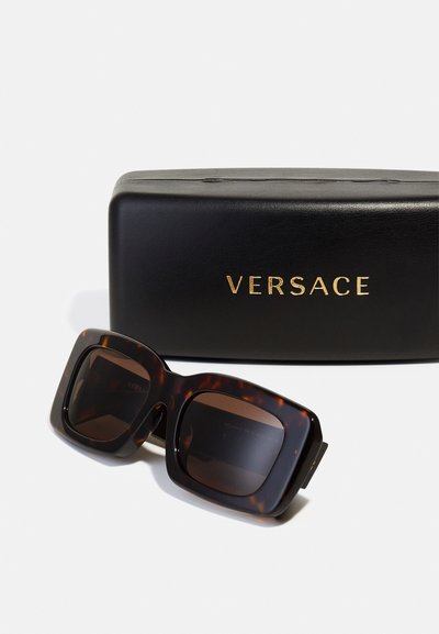 Versace solbriller i skjellmønster med firkantede rammer, mørke glass og gullmerke på et svart hardcase.
