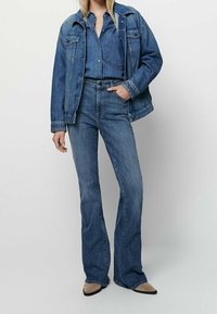 Denim-takki yhdistettynä samaan denim-paitaan ja leveälahkeisiin denim-farkkuihin. Kaikki vaatekappaleet keskitason sinisessä pesussa. Mukana etupockets ja sauman yksityiskohtia.