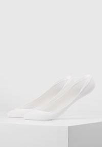 Hvite ballettsko med en glatt, teksturert overflate, rund tå og elastisk bak. Minimalistisk design uten synlig hardware.