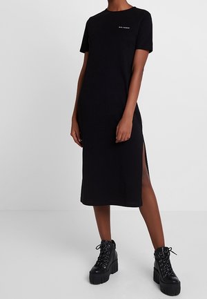 Mujer con vestido midi negro con abertura lateral y texto "Girl Power", combinado con botas negras de plataforma con cordones.