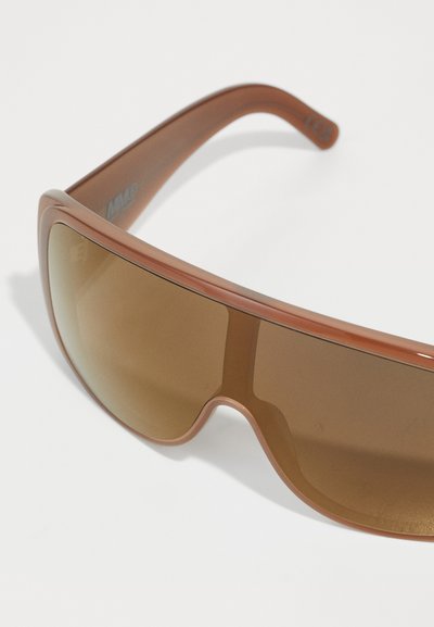 Des lunettes de soleil teintées marron avec une monture en plastique épaisse et arrondie. Les verres sont grands et se courbent légèrement pour une meilleure protection.