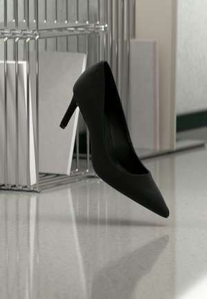 Czarny but na wysokim obcasie balansujący na pięcie na lustrzanej powierzchni obok metalowych organizerów na dokumenty z białymi teczkami.