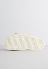 Sandal with a textured white rubber sole, featuring a peach-colored upper strap. The sole has circular indentations for traction.