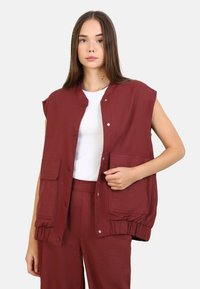 Burgunderröd ärmlös väst med rund halsringning, tryckknappar och två framfickor; textil med struktur och elastiska manschetter.
