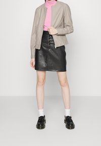 Veste en cuir beige avec fermeture éclair à l'avant, au design cintré ; jupe en cuir noire avec détails de boutons ; chaussures noires avec des glands ; chaussettes blanches.