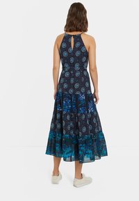 Ärmelloses navy Kleid mit kreisförmigen blauen und türkisfarbenen Mustern, einem Schlüsselloch-Ausschnitt am Rücken, einem gestuften Volantsaum und einem fließenden Design.