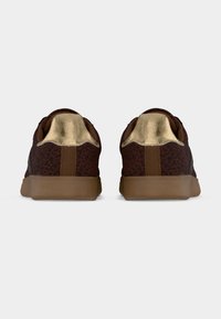 Ζευγάρι καφέ αθλητικά παπούτσια με σκούρο λεοπάρ μοτίβο και μεταλλικές χρυσαφένιες λεπτομέρειες στη φτέρνα, εμφανιζόμενα από πίσω σε απλό φόντο.