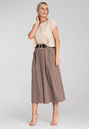 Beige kurzärmliges Oberteil mit Rundhalsausschnitt, kombiniert mit hochtaillierten, plissierten braunen Culottes und einem breiten schwarzen Gürtel mit einer goldenen Schnalle.