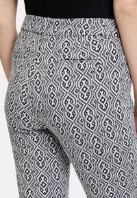 Pantaloni in tessuto bianco con motivi geometrici neri, dotati di due tasche posteriori e un design aderente con finitura testurizzata.