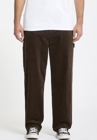 Brune kordfløjspants med lige pasform, sidelommer og blød tekstur, parret med sorte sneakers og en hvid t-shirt.