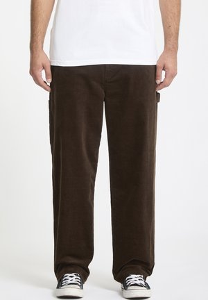 Bruine corduroy broek met een rechte pasvorm, zijzakdetails en een zachte textuur, gecombineerd met zwarte sneakers en een wit t-shirt.