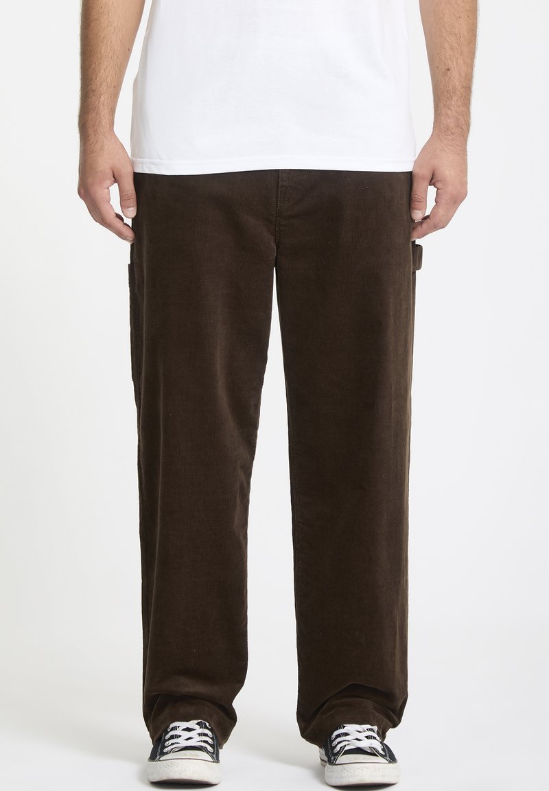 Pantalon en velours côtelé marron avec une coupe droite, détails de poches latérales et texture douce, assorti avec des baskets noires et un t-shirt blanc.
