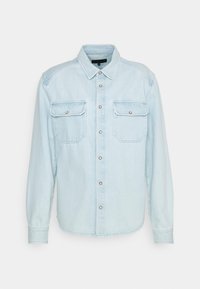 Camicia in denim azzurro chiaro con maniche lunghe, con bottoni davanti, due tasche sul petto e colletto classico. Presenta accessori in tonalità argento.