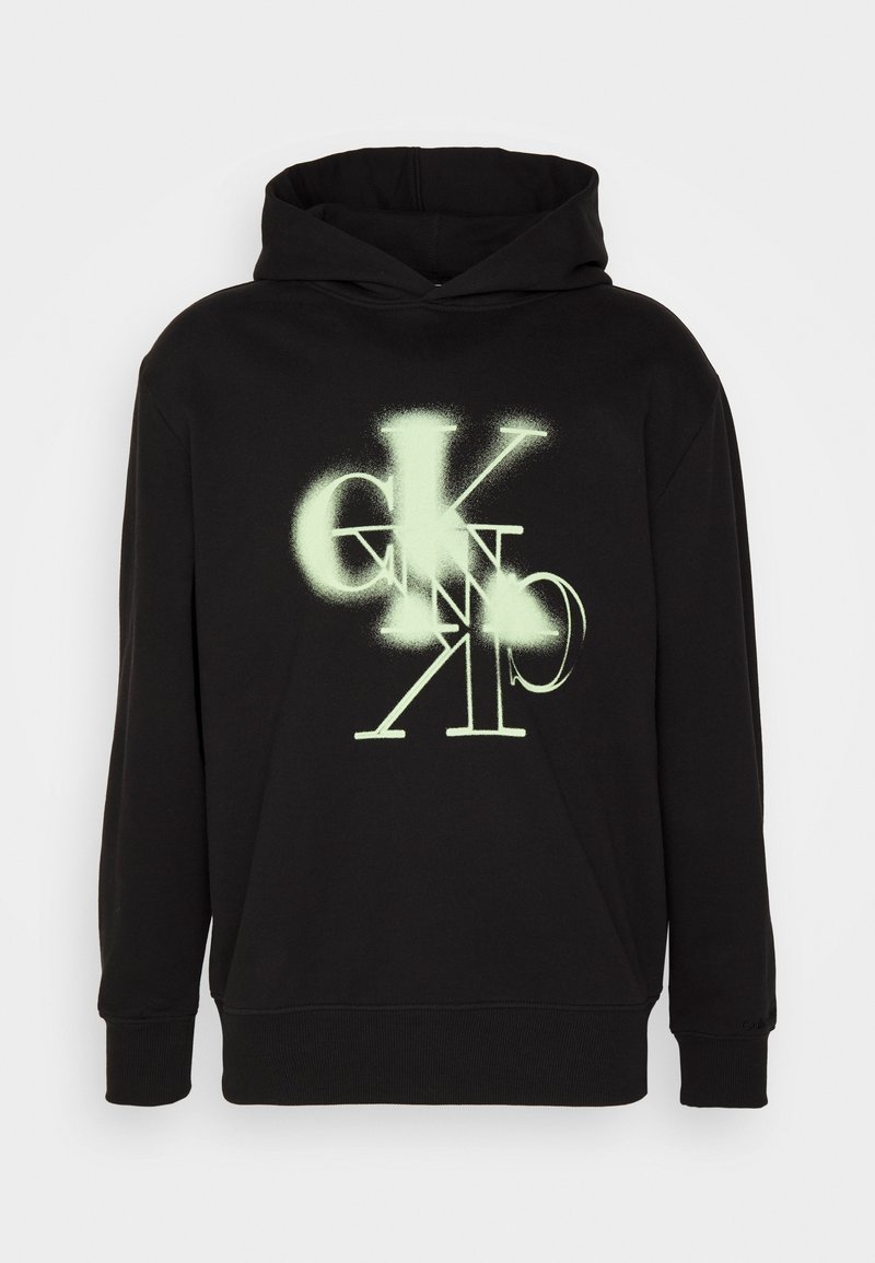 Sweat à capuche noir avec une poche avant et des lettres vert néon superposées "CK" dans un style aérosol centrées sur la poitrine.