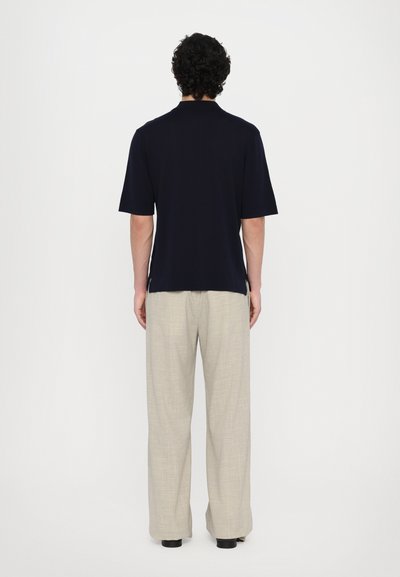 Polo bleu marine à manches courtes avec une coupe décontractée, associé à un pantalon large en lin beige. Texture lisse, fentes latérales à l'ourlet.