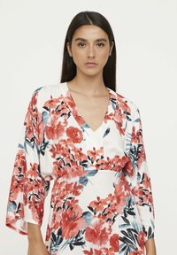 Blumenkleid mit V-Ausschnitt, weißem Hintergrund und roten sowie petrolfarbenen Blumen. Lange, weite Ärmel mit einem gerafften Taillendesign.