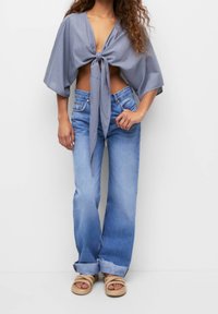 Haut court gris noué avec un décolleté profond, associé à un jean évasé bleu clair et des sandales en corde beige. Design simple, textures de tissu décontractées.