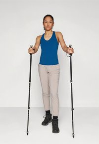 Atlétikai ruházat, amely kék ujjatlan felsőből és világos bézs nadrágból áll. A figura fekete túrabotokkal és fekete túracipővel van felszerelve.