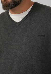 Dunkelgrauer V-Ausschnitt-Pullover aus Strickstoff, mit einem dezenten s.Oliver-Logo auf der Brust, übereinander getragen mit einem weißen Hemd.