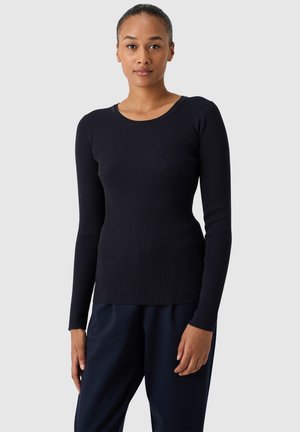 Maglietta a maniche lunghe a coste in blu navy, colletto rotondo, design aderente, tessuto testurizzato, abbinata a pantaloni scuri a vestibilità rilassata.