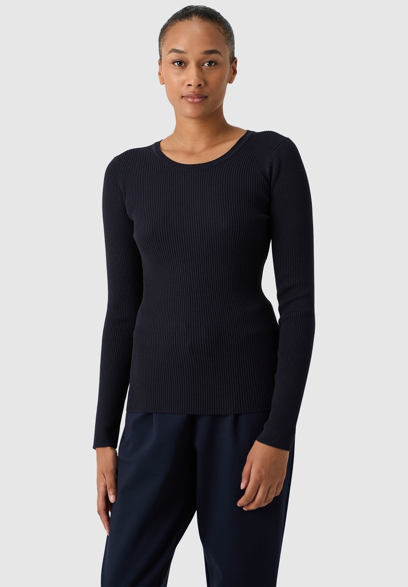 Maglietta a maniche lunghe a coste in blu navy, colletto rotondo, design aderente, tessuto testurizzato, abbinata a pantaloni scuri a vestibilità rilassata.