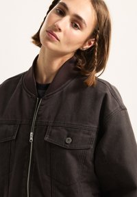 Dunkelbraune Bomberjacke mit geripptem Kragen, Reißverschlussschluss und zwei Fronttaschen. Hergestellt aus strukturiertem Stoff mit lockerer Passform.