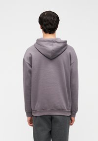 Φούτερ με κουκούλα σε απαλό γκρι χρώμα, με χαλαρή εφαρμογή, ριμπ τελείωμα και μαλακή υφή υφάσματος. Η πίσω όψη δεν παρουσιάζει επιπλέον λεπτομέρειες.