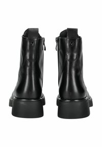 Un par de.botines de cuero negro con tiradores, cremalleras laterales, tacones en bloque elevados y un pequeño logo circular en la parte superior trasera.