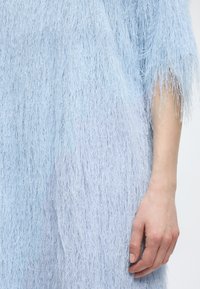 Κοντινό πλάνο ενός ανοιχτό μπλε υφασμάτινου φορέματος με υφή και λεπτές ίνες, με εμφανές το ακάλυπτο δεξί χέρι και το χαλαρό χέρι.