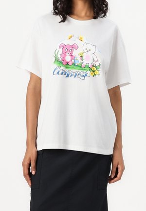 T-shirt en coton blanc présentant un graphisme coloré d'un lapin rose et d'un chat blanc parmi des fleurs, avec le texte "Converse" en bleu en dessous.