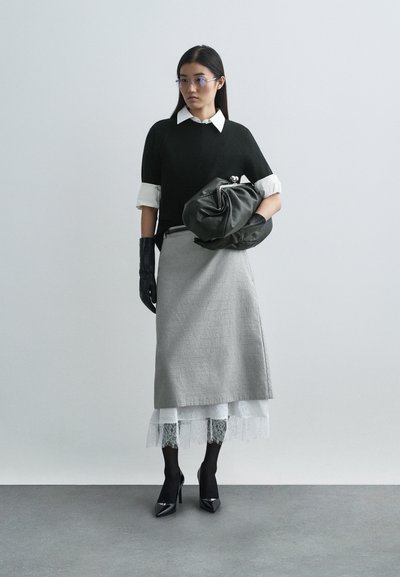 Black knit sweater over a white collared shirt, gray skirt with lace trim, black gloves, and pointed black heels, holding a dark bag.