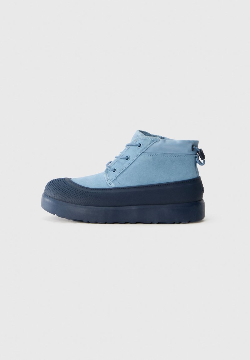 Baskets montantes bleues avec semelle en caoutchouc épais bleu foncé et embout, lacets à l'avant et lanière au talon sur fond uni.