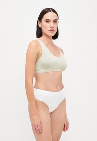 Bralette verde claro sem costura com alças largas e uma textura suave. Combinado com um fundo de biquini branco de cintura alta. Design simples.