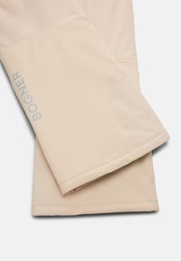 Beige bunda Bogner, rukávy s viditelným prošitím a reflexní logo na levém rukávu na bílém pozadí.