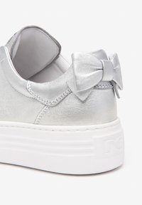 Baskets argentées avec une finition métallique lisse, arrière arrondi, semelle plate blanche et un nœud décoratif sur le talon.