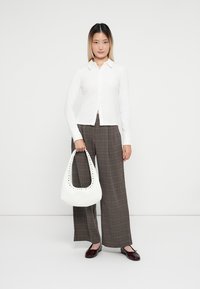Cămașă albă cu guler, pantaloni largi cu carouri maro, și o geantă albă cu detalii cu piulițe, completată de balerini burgundy.
