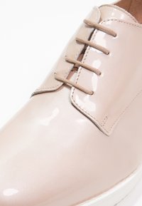 Chaussure beige brillante à lacets avec trois œillets et un bout arrondi lisse, vue en gros plan.