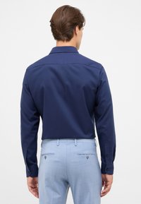 Marineblauw shirt met lange mouwen, een standaardkraag, een gladde textuur en manchetten met knopen, gecombineerd met lichtblauwe broek met achterzakken.
