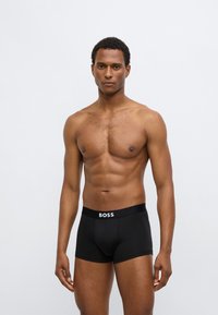 Boxers noirs avec une large ceinture élastique arborant la marque blanche "BOSS". Tissu lisse, coupe ajustée, adapté à un usage décontracté.