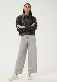 Sort læder cropped jakke med sølvnitter, parret med løse grå denim bukser og hvide sneakers. Jakken har frontlommer og en krave.
